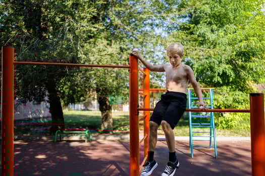 Athletic teenager sits on the crossbar, holding on to the handrail. Street workout on a horizontal bar in the school park. photo