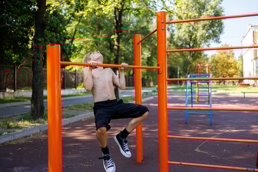 The teenager is heavily pulled out on the crossbar. Street workout on a horizontal bar in the school park. photo