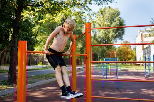 The teenager holds his weight on outstretched arms while performing elements on the crossbar. Street workout on a horizontal bar in the school park. photo