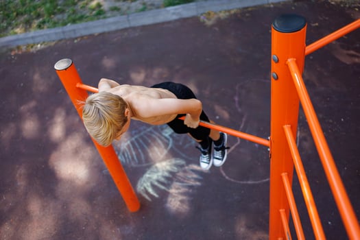 A teenager stretched out holding onto his arms and performing acrobatic exercises on a horizontal bar. Street workout on a horizontal bar in the school park. photo