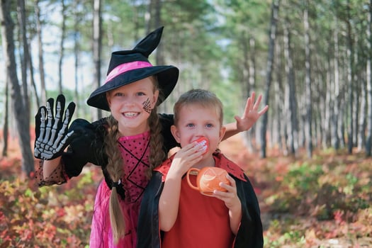 Funny kids in carnival costumes outdoors. A girl dressed as a witch and a boy in a Halloween costume scare looking at the camera. photo