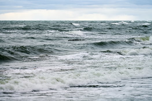 View of blue sea with foaming waves and wooden breakwaters photo