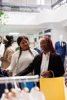African american women shopping for clothes and chatting in mall. Girlfriends customers searching for apparel hanging on rack and choosing outfit together in fashion boutique photo