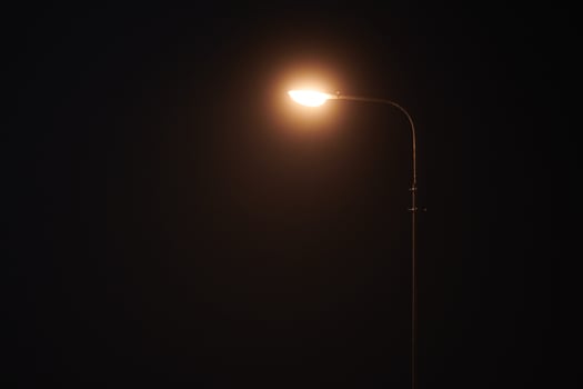One night lamppost shines with faint mysterious yellow light through evening fog, copy space photo