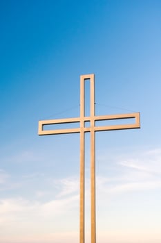 Golden cross against a background of blue sky with clouds. A minimalistic view of a gold-colored cross against the sky. photo