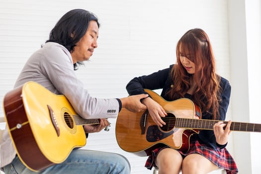 Young Asian teenager is learning to play guitar by professional teacher who showing simple chords for music class school photo