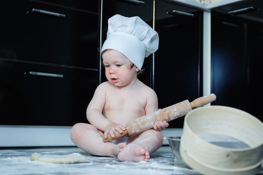 Little boy sitting on carpet in kitchen playing with cooking pots. Cute boy cooking in kitchen at home photo
