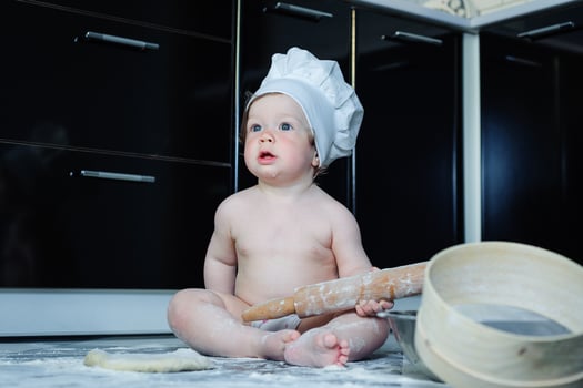 Little boy sitting on carpet in kitchen playing with cooking pots. Cute boy cooking in kitchen at home photo