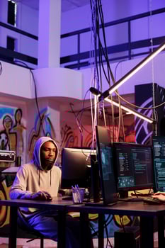 African american criminal hacking into server and cracking password on computer. Hacker breaching cybersecurity system and doing illegal crime activity late in abandoned warehouse photo
