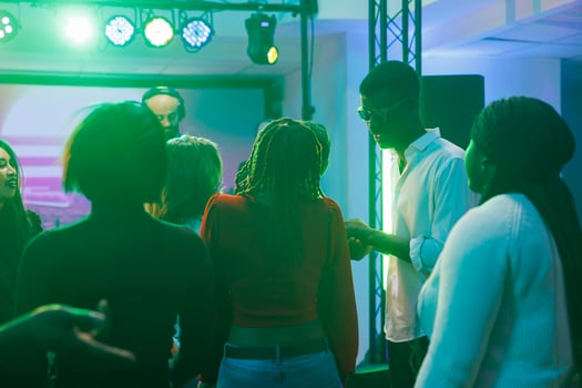 People partying and having fun at social gathering while attending dj concert in nightclub. Diverse crowd relaxing on dancefloor while musician performing on stage in dark club photo