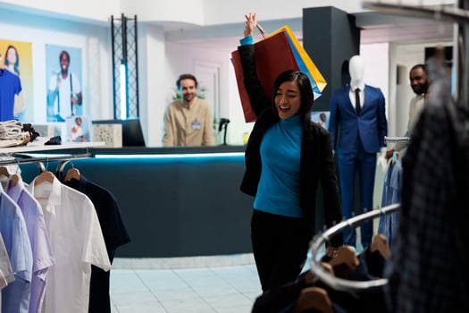 Happy woman making dance moves with shopping bags after buying garment in clothing store. Fashion boutique smiling asian customer raising hand with paper packages of purchases photo
