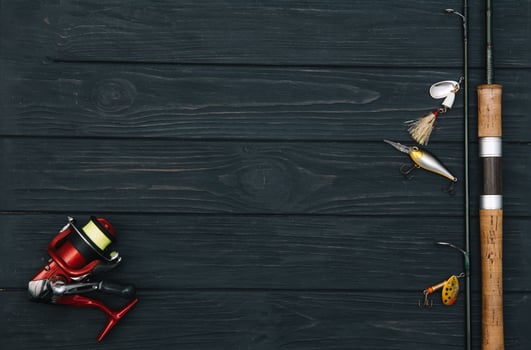 Fishing tackle - fishing spinning, hooks and lures on darken wooden background. Top view. photo