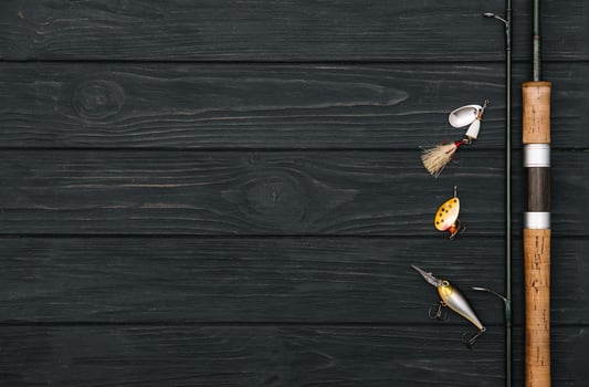 Fishing tackle - fishing spinning, hooks and lures on darken wooden background. Top view photo