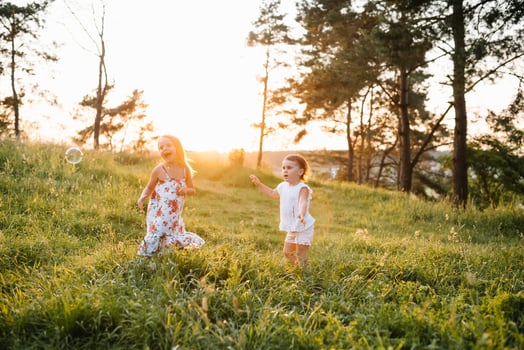 Little sisters girls having fun in the summer forest, sitting on the blanket and smiling photo