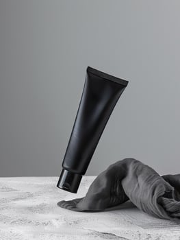 A black tube of face cream is suspended in mid-air above a gray cloth. photo