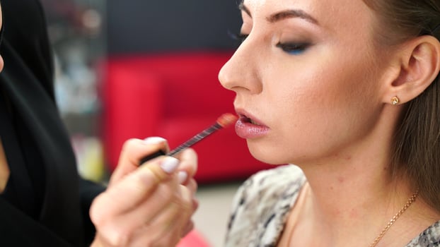 A woman is getting her lips painted by a man. The woman is wearing a black shirt and the man is wearing a white shirt. photo