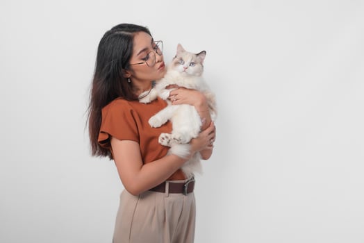Portrait of young Asian woman in brown shirt holding her ragdoll cat and making kiss pouty face isolated over white background. photo
