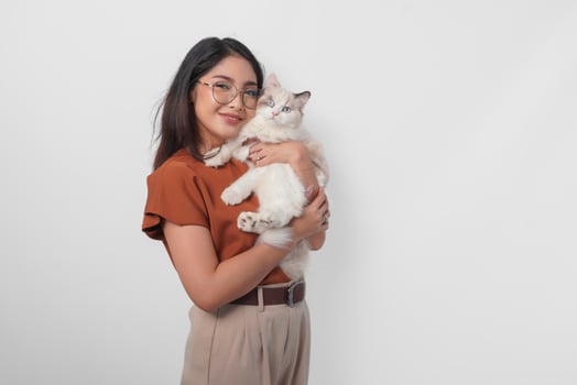 Portrait of young Asian woman in brown shirt holding her ragdoll cat and smiling to the camera isolated over white background. photo