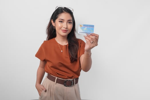 Confident young Asian woman wearing brown shirt is showing identity card Indonesia to the camera over white background. photo