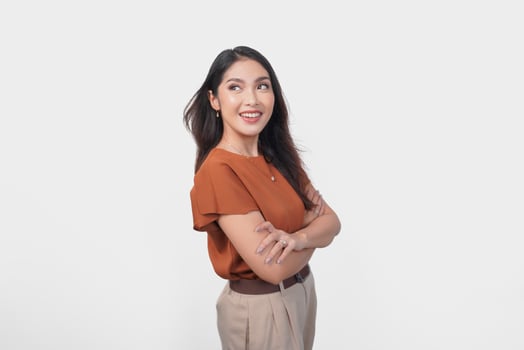 Charming young Asian woman in brown t-shirt looking or peeking at the top with crossed arms over isolated white background. photo