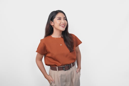 Charming young Asian woman in brown t-shirt looking or peeking at the top with crossed arms over isolated white background. photo