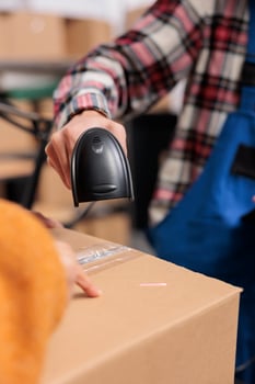 Warehouse employee scanning cardboard box barcode while doing inventory control. Delivery service operator managing parcel receiving and checking qr code with scanner close up photo