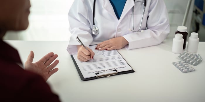 Doctor consulting male elderly patient filling medical form. Professional physician writing information in clipboard checking examining elderly man during appointment visit in clinic photo