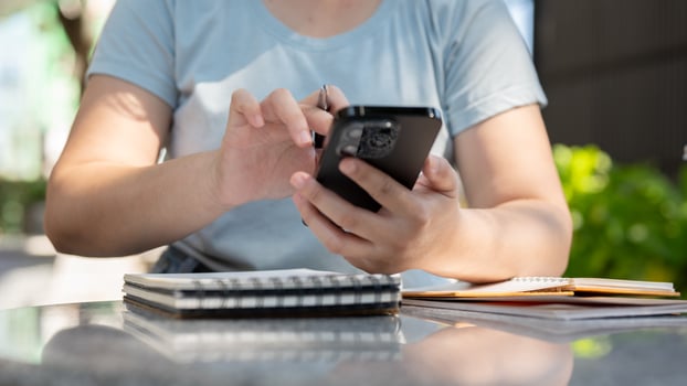 A woman sitting at an outdoor table, reading information on her phone while working remotely. photo