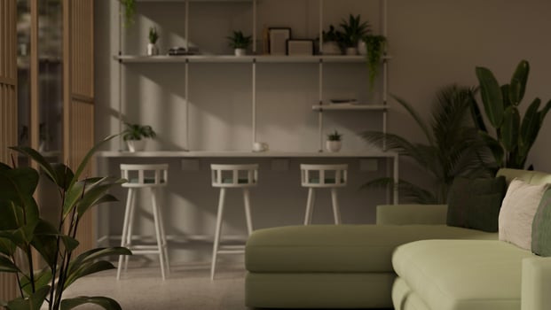 A modern lounge seating area features a green sofa, a table with stools, and houseplants. photo