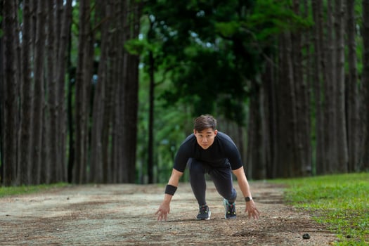 Asian trail runner is running outdoor in pine forest dirt road for exercise and workout activities training while concentrate on the start position to race for healthy lifestyle and fitness concept photo