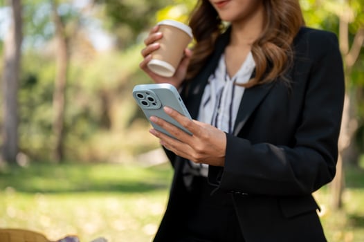 A businesswoman is sipping coffee and checking messages on her smartphone while relaxing in a park. photo