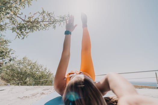 Fitness woman sea. Happy middle aged woman in orange sportswear exercises morning outdoors on yoga mat with laptop in park over ocean beach. Female fitness pilates yoga routine. Healthy lifestyle. photo