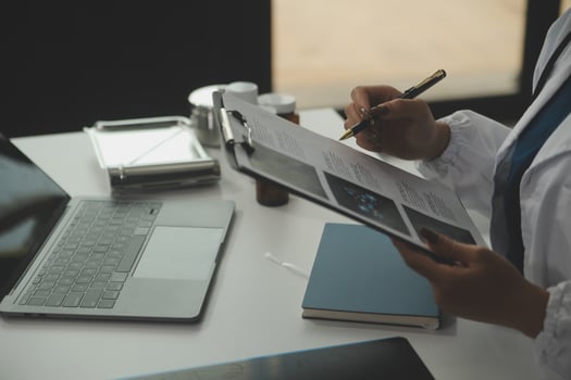 Serious female doctor using laptop and writing notes in medical journal sitting at desk. Young woman professional medic physician wearing white coat and stethoscope working on computer at workplace. photo