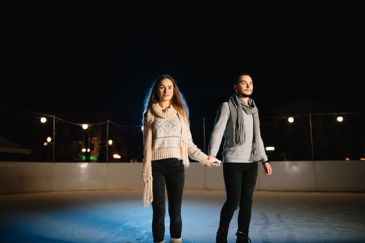 Winter skates, loving couple holding hands and rolling on rink. Illumination in background, night. Concept training. photo