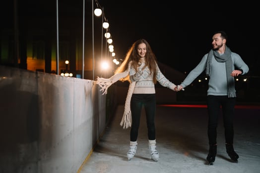 Man and woman young family Happy smiles hold hands skate on winter rink at night, with bokeh lights. photo