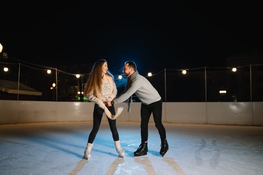 Winter skates, loving couple holding hands and rolling on rink. Illumination in background, night. Concept training. photo