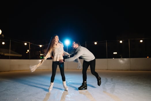 Man and woman young family Happy smiles hold hands skate on winter rink at night, with bokeh lights. photo