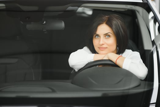 Young woman smiling in her new car in a showroom photo