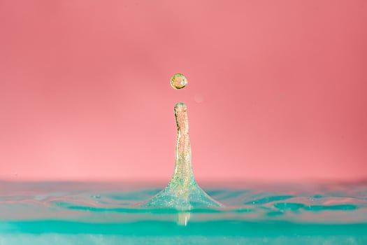golden Water droplets fall down closely into the blue water, on pink background, colorful concept of concept of beauty, luxury photo