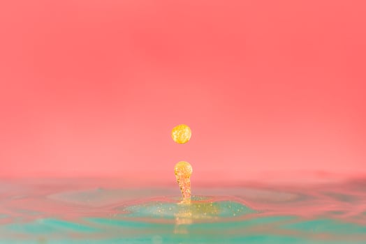 golden Water droplets fall down closely into the blue water, on pink background, colorful concept of concept of beauty, luxury photo