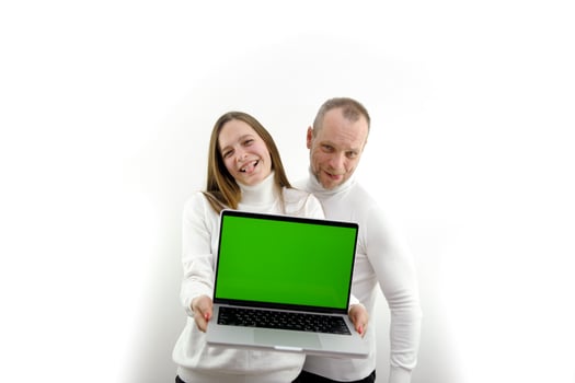 father and adult daughter show laptop with blank screen space for text girl shows tongue smiling fun joy joke white background white clothes Silver laptop chroma key green screen photo