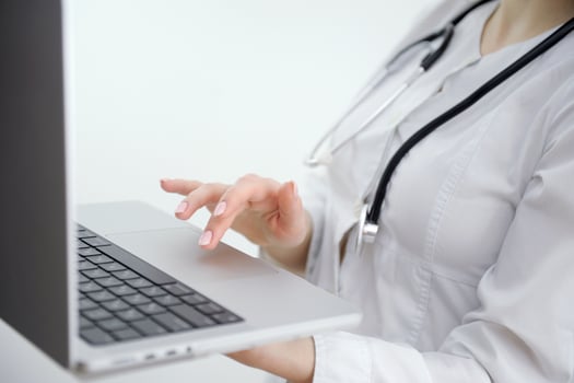 Close up of unknown female doctor sitting at the table near the window in hospital and typing at laptop computer photo