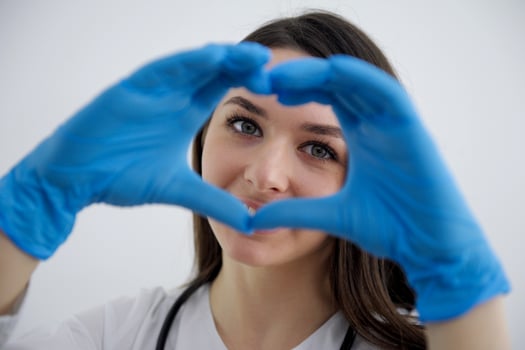 Smiling beautiful young indian ethnicity female doctor cardiologist showing heart symbol with fingers, expressing love and support to patients, healthcare medical help charity donation concept. photo