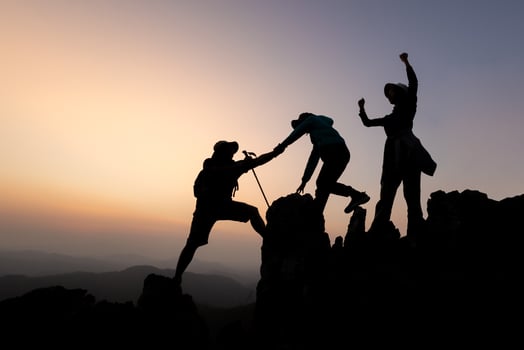 Silhouette of person hikers climbing up mountain cliff and one of them giving helping hand. People success, team work concept. photo