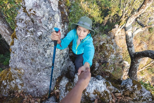 Person women hikers climbing up mountain cliff and one of them giving helping hand. People success, team work concept. photo