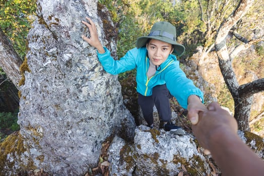 Person women hikers climbing up mountain cliff and one of them giving helping hand. People success, team work concept. photo