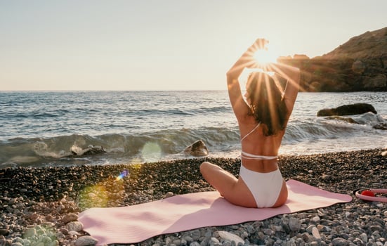 Woman sea yoga. Happy woman in white swimsuit and boho style braclets practicing outdoors on yoga mat by sea on sunset. Women yoga fitness routine. Healthy lifestyle, harmony and meditation photo