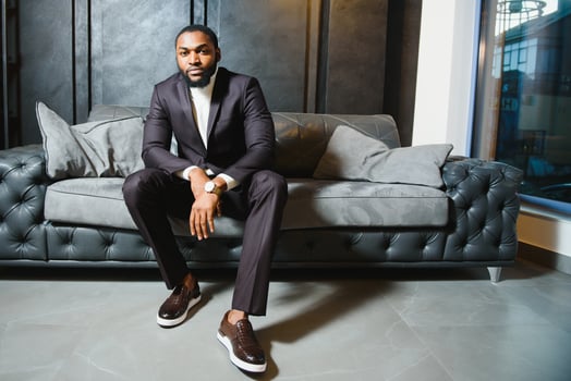 Young black man in suit on dark background sitting on a sofa. Fashion portrait of young man. photo