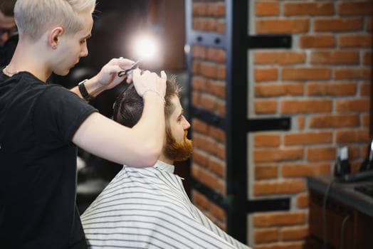 Making haircut look perfect. Young bearded man getting haircut by hairdresser while sitting in chair at barbershop. photo