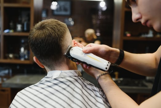 Making haircut look perfect. Young bearded man getting haircut by hairdresser while sitting in chair at barbershop. photo